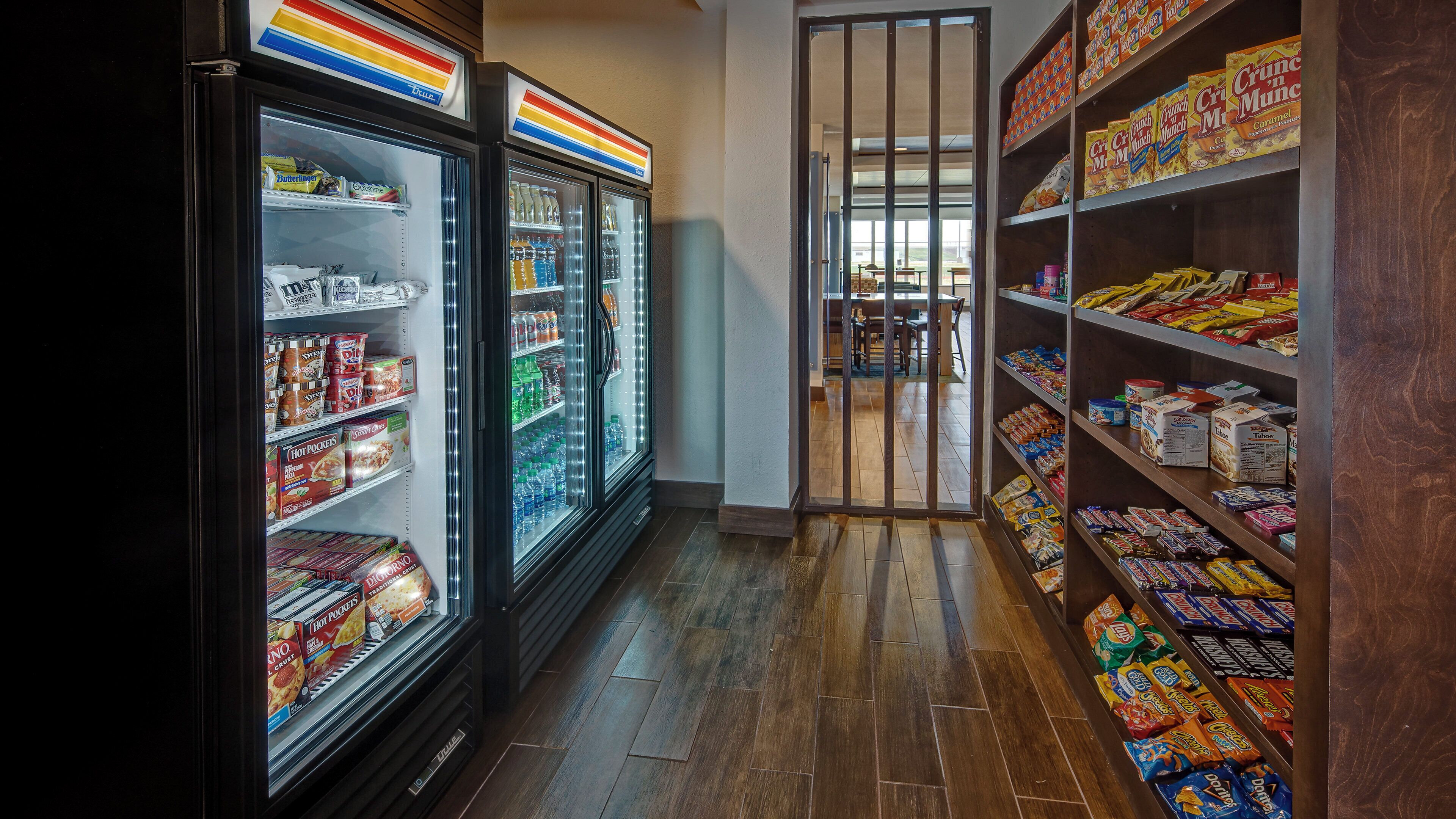 Passadeira de supermercado com seções refrigeradas à esquerda e prateleiras repletas de lanches e bebidas à direita.