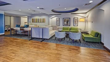 Un hall de hotel con mostrador de recepción, zona de estar con sillas y sofás, alfombra estampada y obras de arte en las paredes.