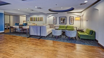 Un hall de hotel con mostrador de recepción, zona de estar con sillas y sofás, alfombra estampada y obras de arte en las paredes.