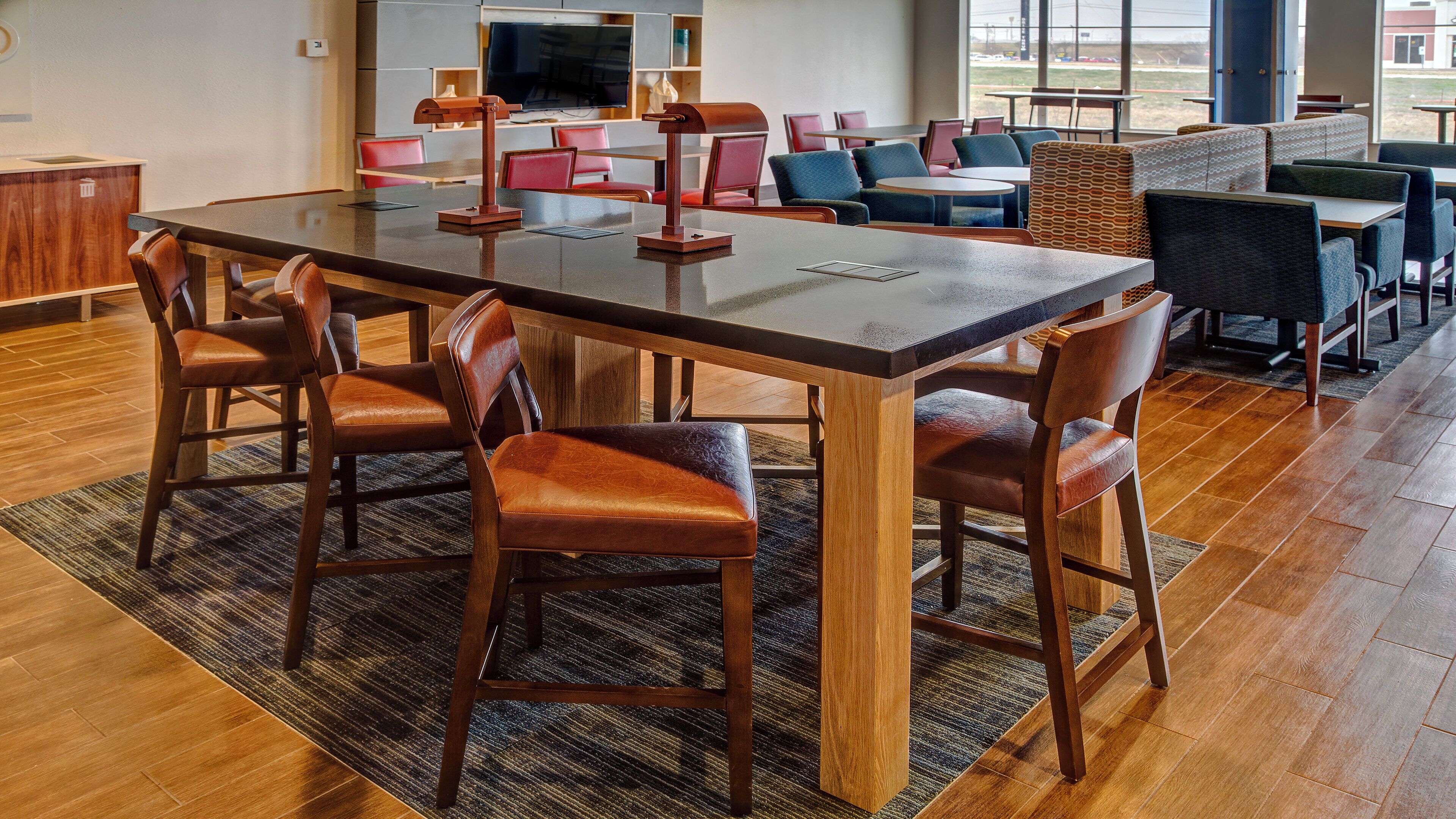 A modern dining area with a long table, leather chairs, and a patterned rug.