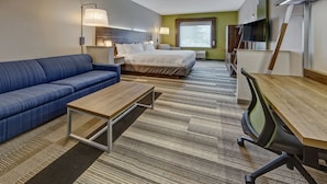 Ein Hotelzimmer mit einem Bett, einem blauen Sofa, einem Holztisch, einem Schreibtisch mit Stuhl und einem Fernseher.
