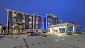 Un hotel con entrada cubierta, un estacionamiento con espacios delimitados y un coche rojo estacionado allí.