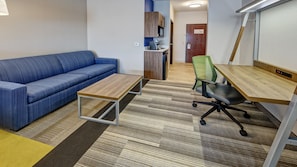 Une petite pièce moderne, avec un canapé bleu, une table en bois et un fauteuil de bureau vert.