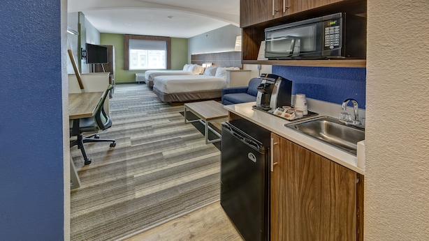Ein Hotelzimmer mit Küchenzeile, einem Bett, einem Schreibtisch und einem Fernseher.