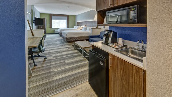 Une chambre d’hôtel équipée d’une kitchenette, d’un lit, d’un bureau et d’une télévision.