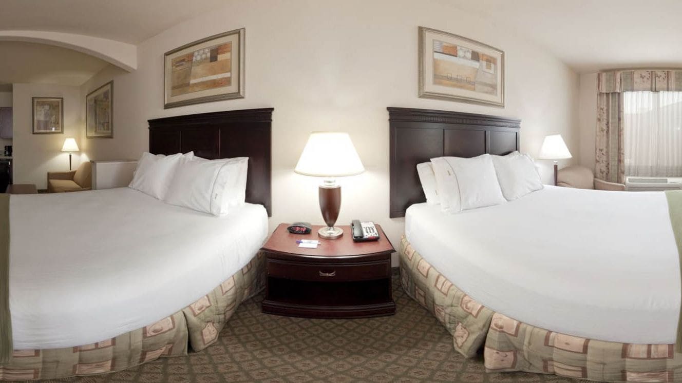 A hotel room with two beds, a nightstand with a lamp, and a small table with a telephone.