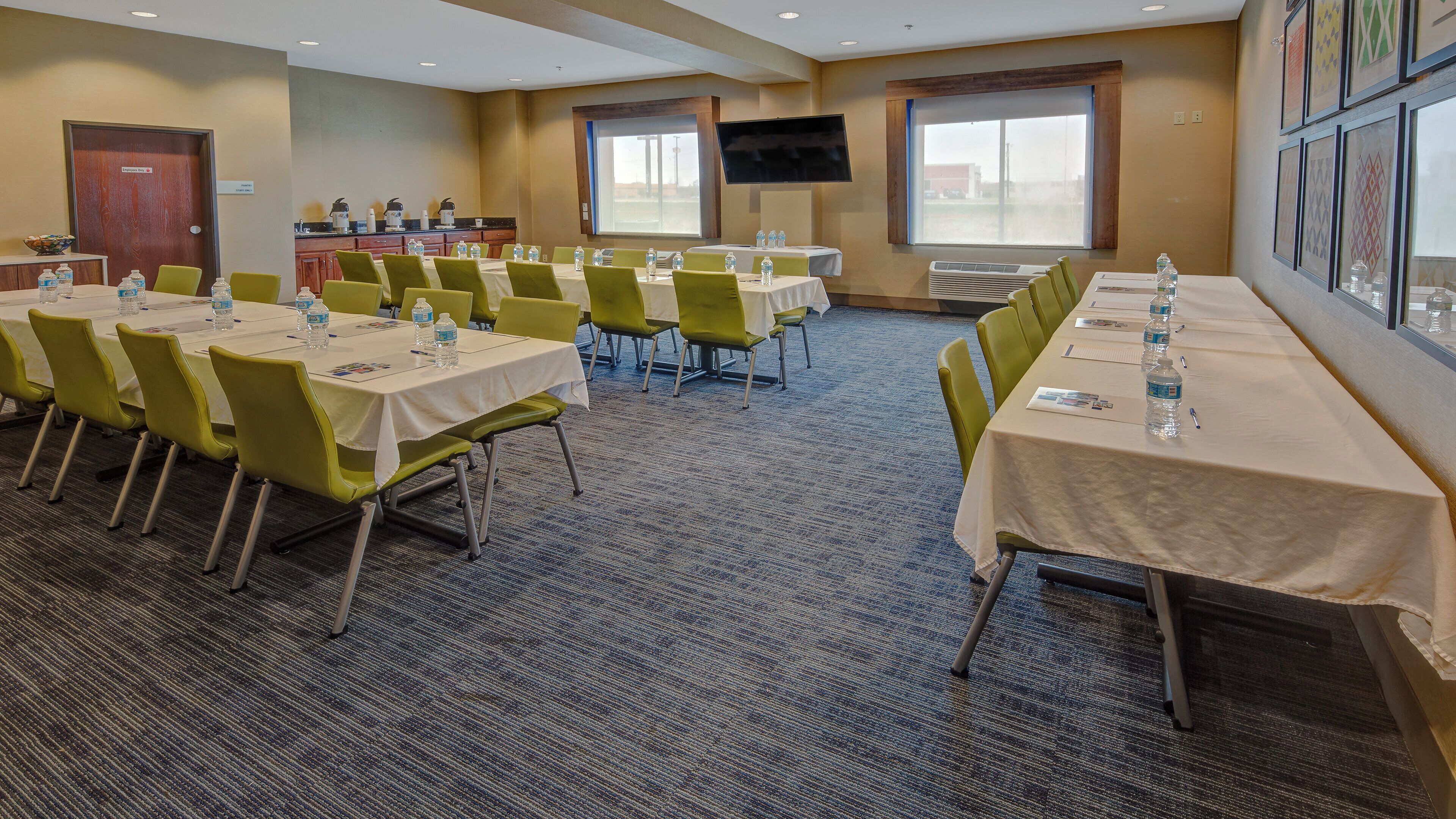 A conference room with tables, chairs, and a television screen.