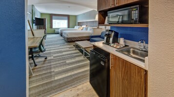 Habitación de hotel con kitchenette, una cama, un escritorio y un ventanal grande.
