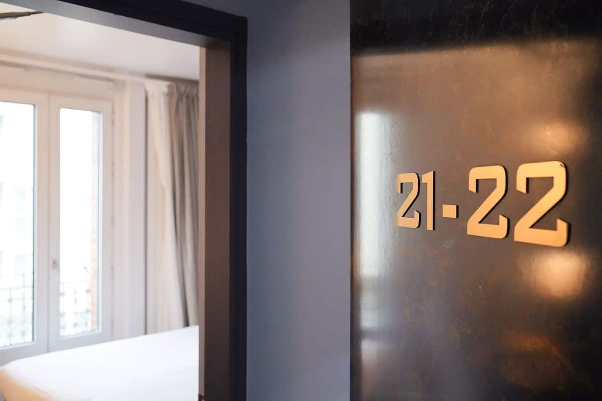 A hotel room with a bed, a window with curtains, and a wall with the numbers "21-22" indicating room numbers.