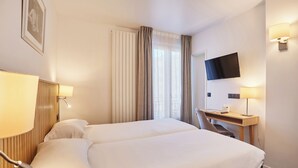 A hotel room with two beds, a desk, a TV, and a window with curtains. - Hôtel Gabriel Issy (Issy-les-Moulineaux)