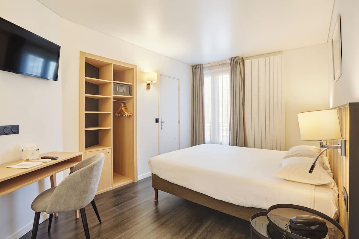 A hotel room with a bed, a desk, a chair, a TV, a lamp, and a wardrobe.