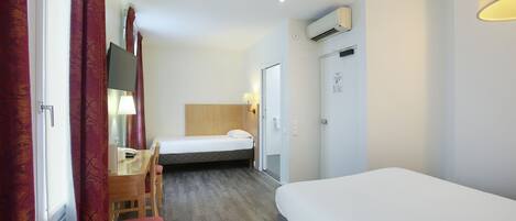 Habitación de hotel con cama, escritorio, silla, lámpara y aire acondicionado.