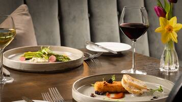 A dining table with plates of food, wine glasses, and a vase with flowers.
