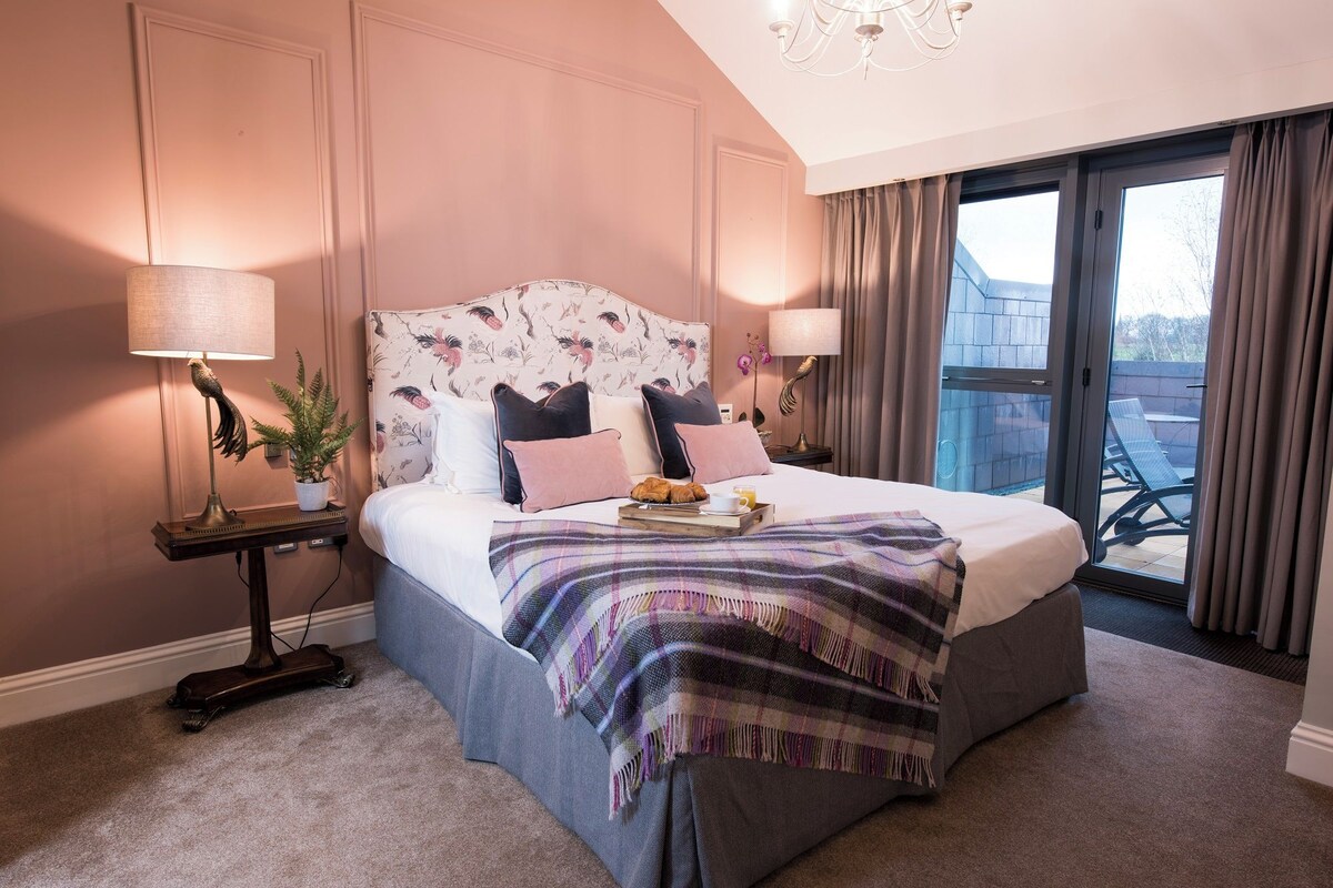 A bedroom with a bed, a nightstand, a lamp, a potted plant, and a view of the outside.