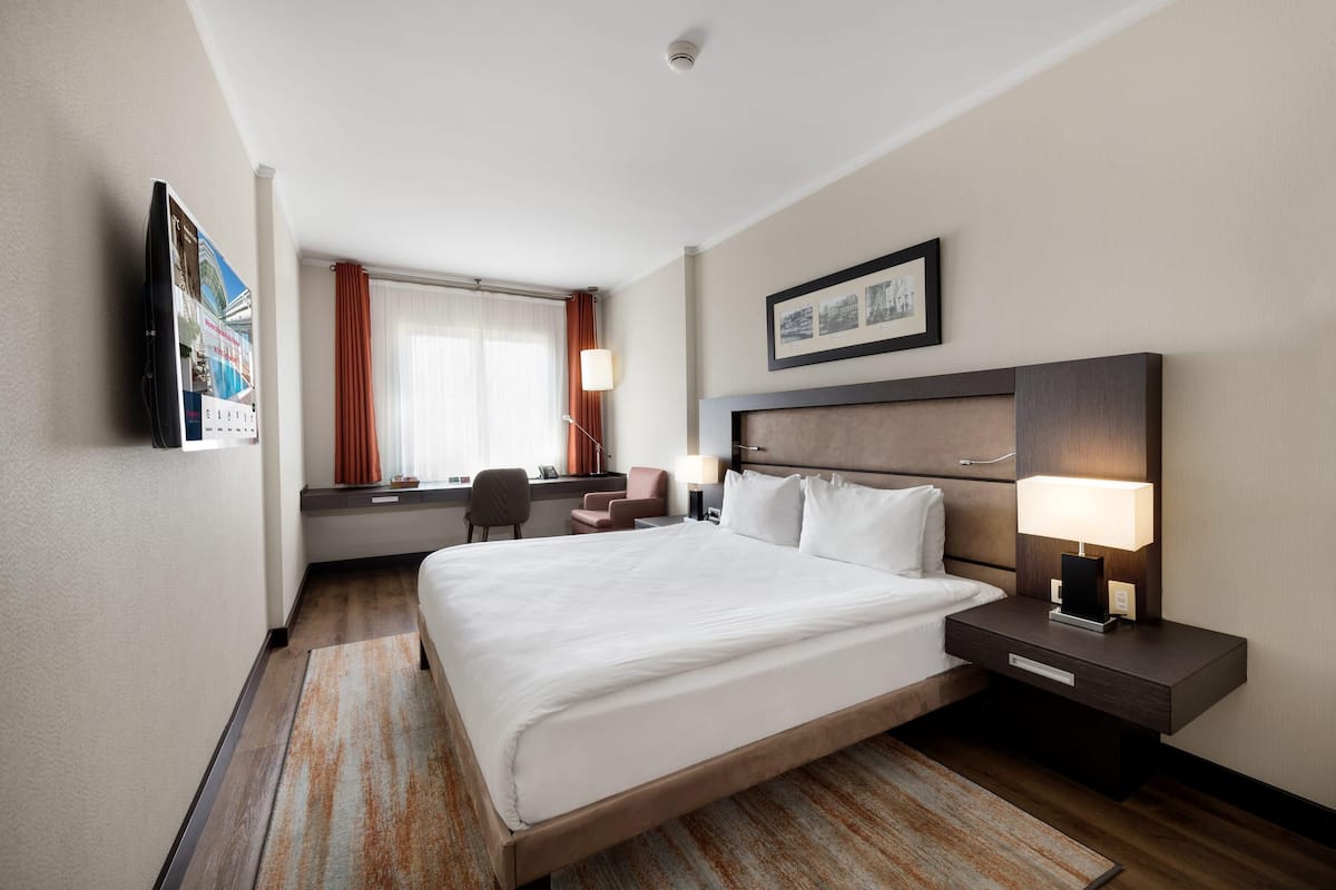 Ein Hotelzimmer mit einem großen Bett, Nachttischen, einem Schreibtisch und einem Stuhl.