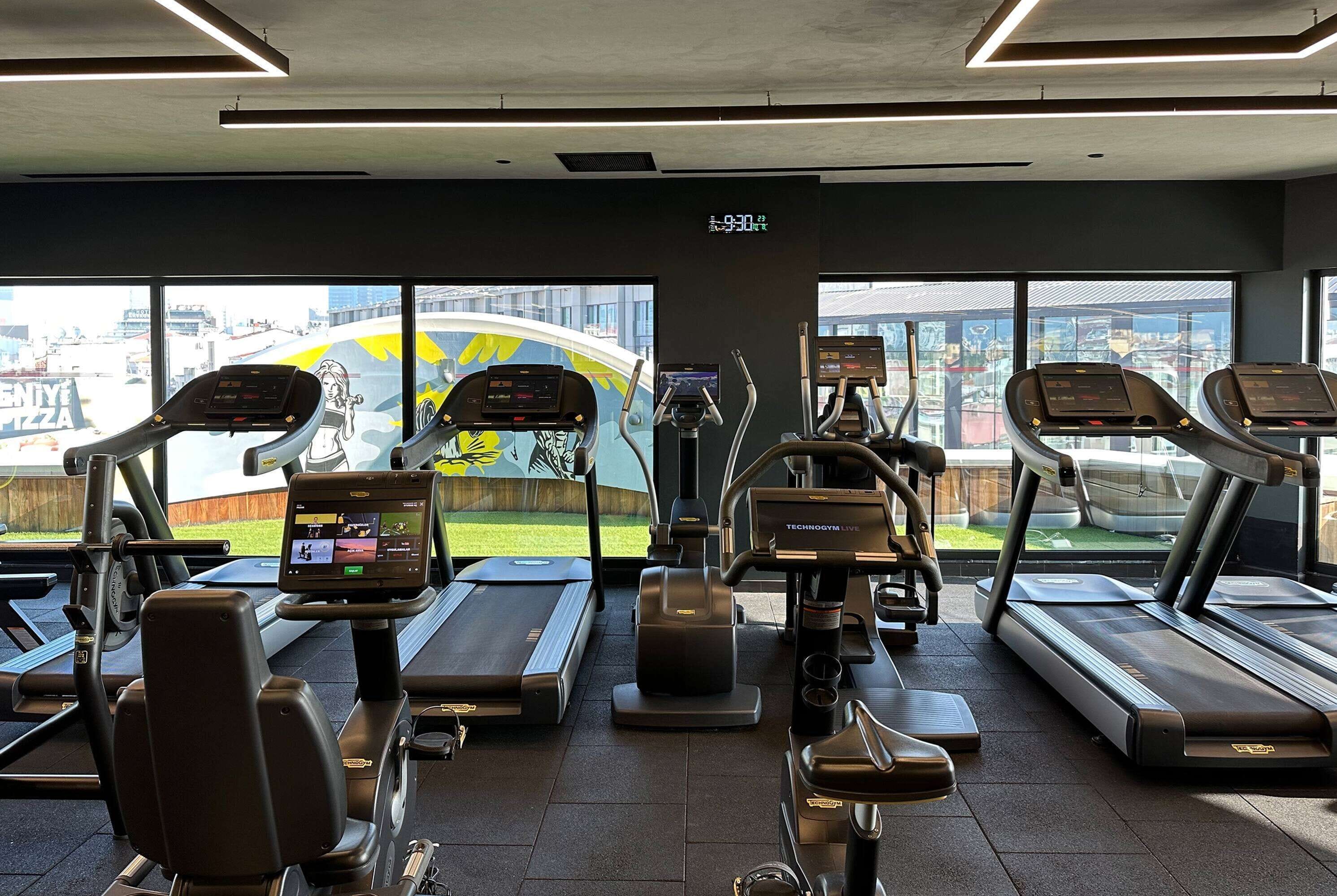 A gym with treadmills, elliptical machines, and a digital display.