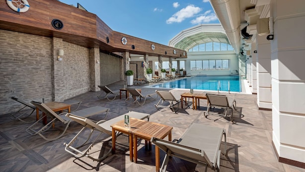 Zona junto a la piscina con sillones de descanso, una mesa de madera y vista al estanque.