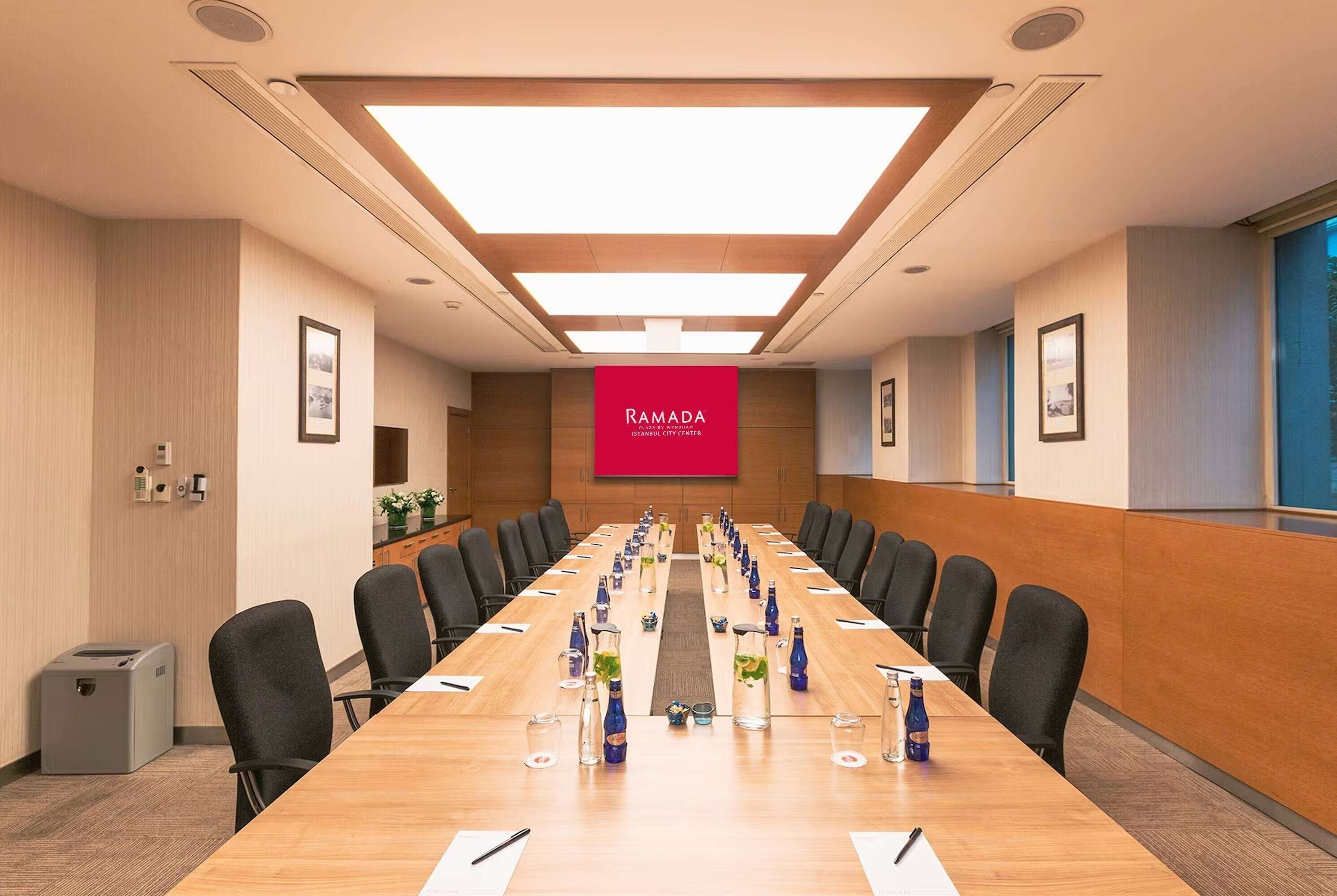A conference room with a long table, chairs, and a large screen displaying 'RAMADA'.