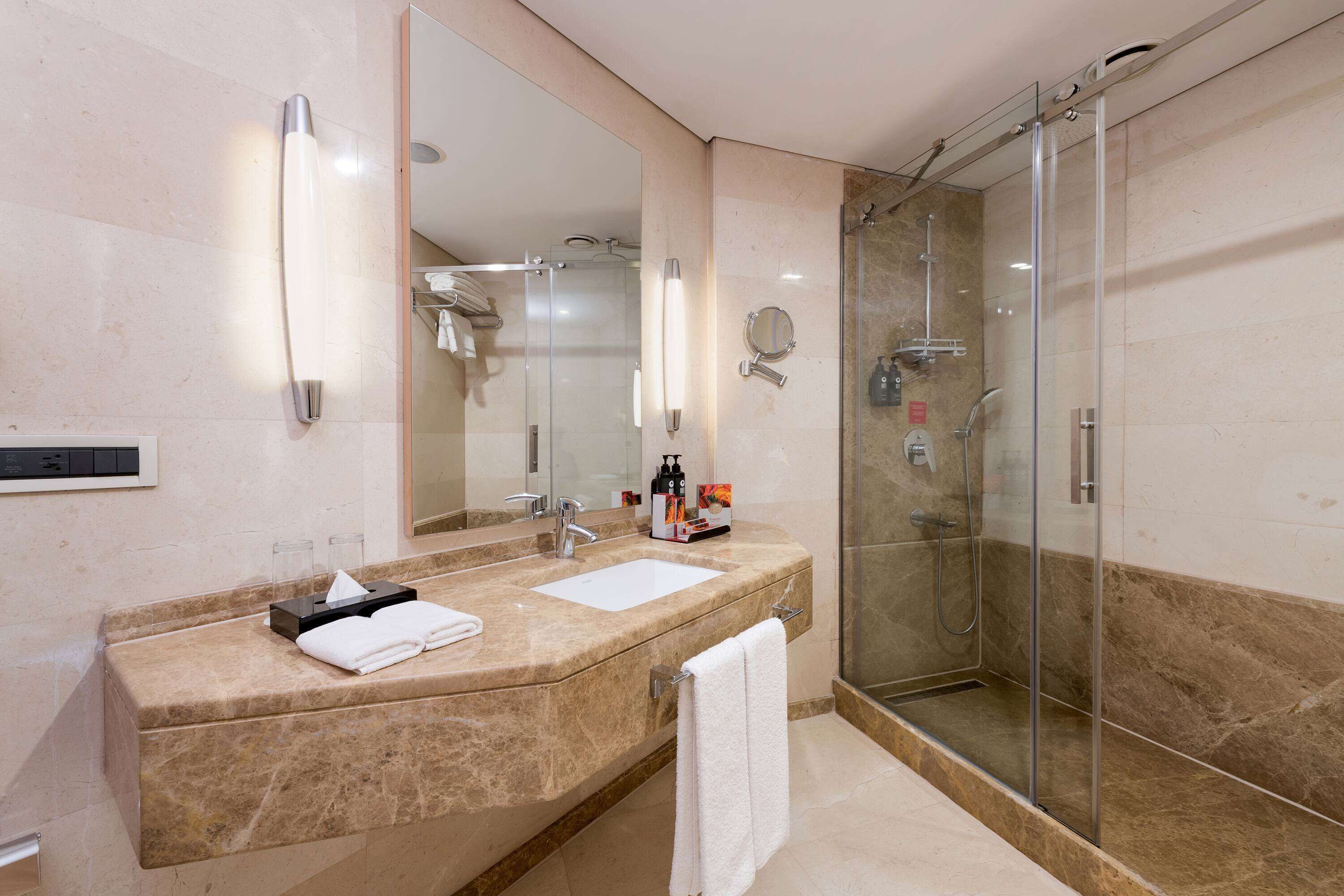 Un baño moderno con un espejo grande, dos lavabos, una cabina de ducha con mampara de cristal y un perchero para toallas.