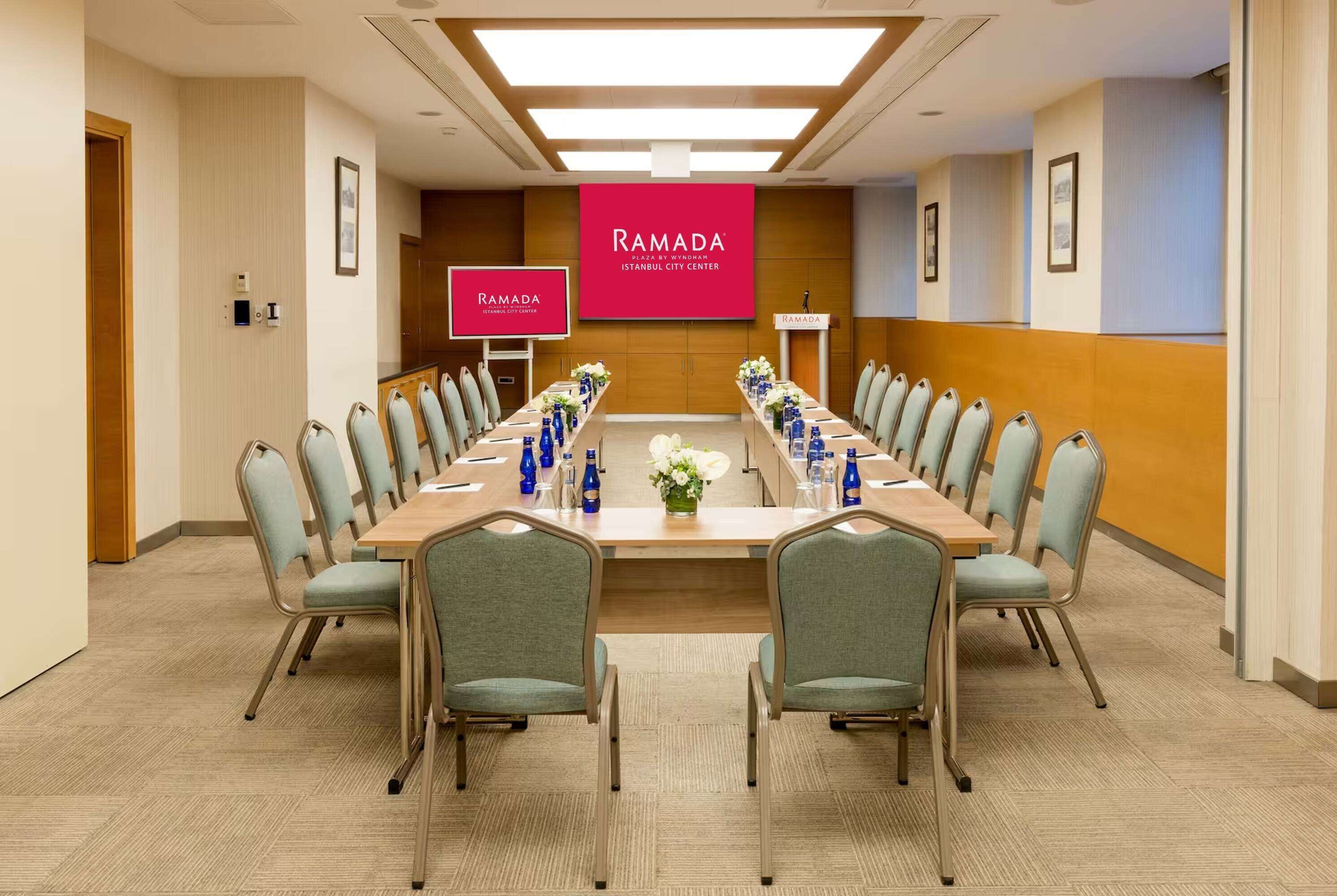 A conference room with a long table, chairs, and a large screen displaying "RAMADA Istanbul City Center".