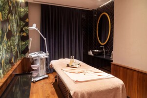 A room with a massage table, a large mirror, a sink, and a wall with a tropical leaf pattern.