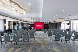 A conference room with rows of chairs, a stage, and a large screen displaying "RAMADA ISTANBUL CENTER".