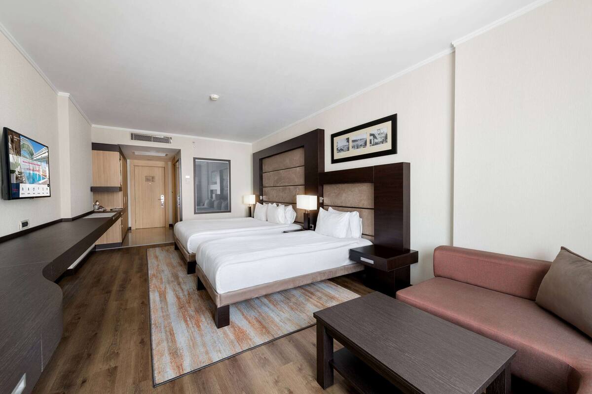 Ein Hotelzimmer mit einem großen Bett, einer Sitzecke, einem Schreibtisch und einer kleinen Küchenzeile.
