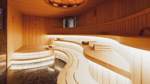 Un intérieur en bois, avec des bancs en bois aux formes arrondies et un luminaire circulaire placé au centre.