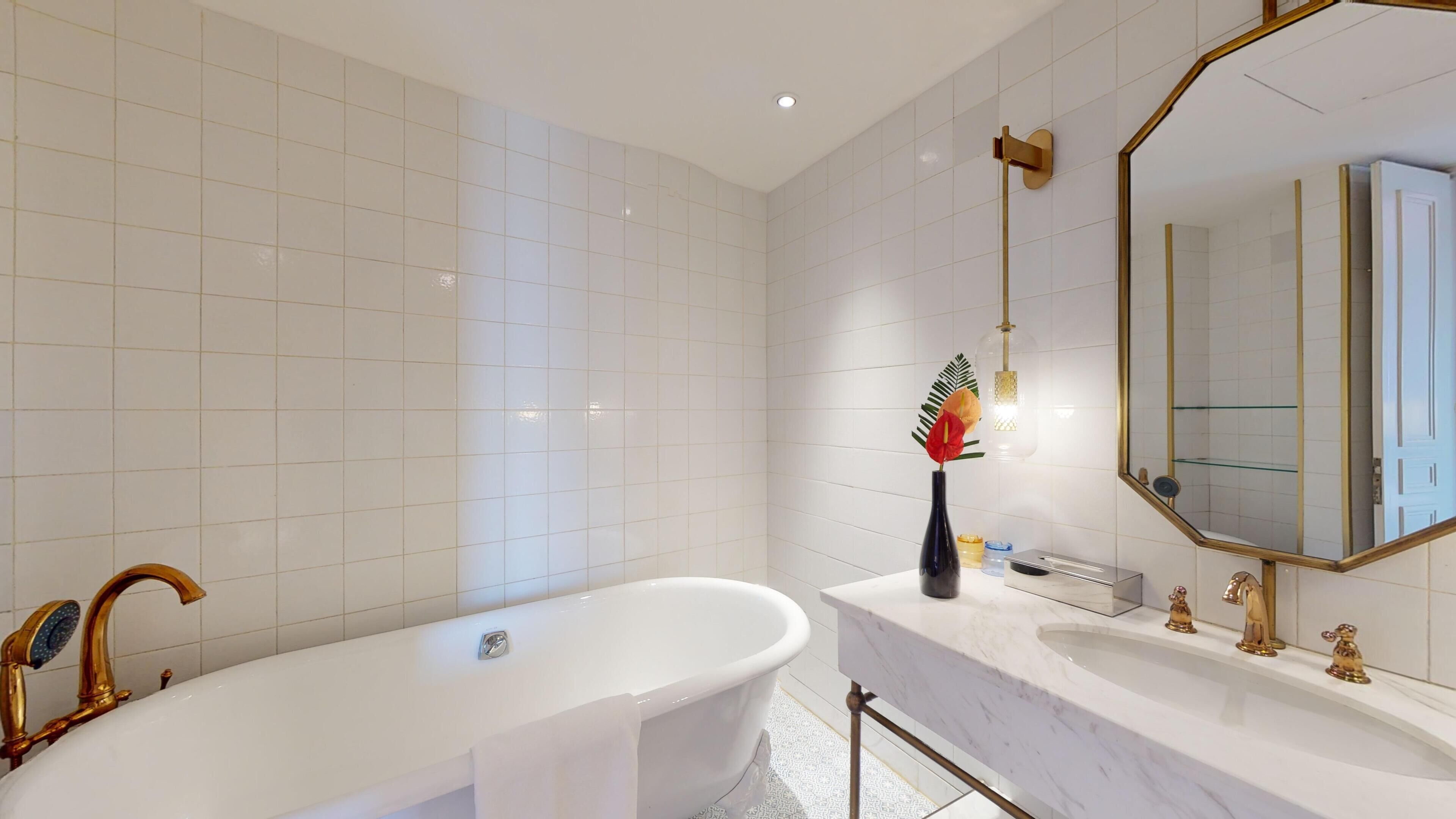 Un baño moderno con una bañera independiente, un espejo grande y un tocador con detalles dorados.