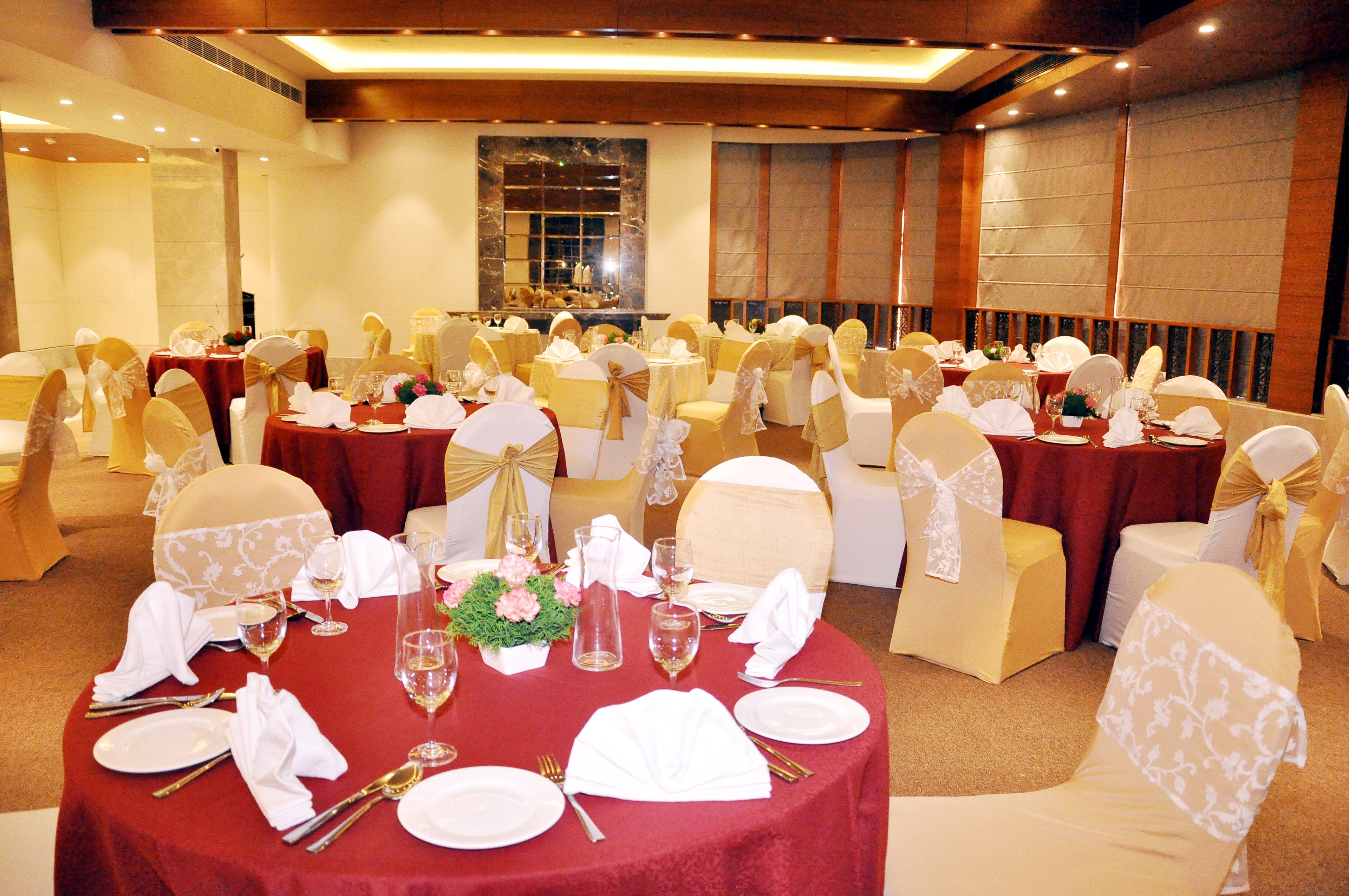 A banquet hall with round tables set for dining, each with white tablecloths, gold sashes, and white napkins.