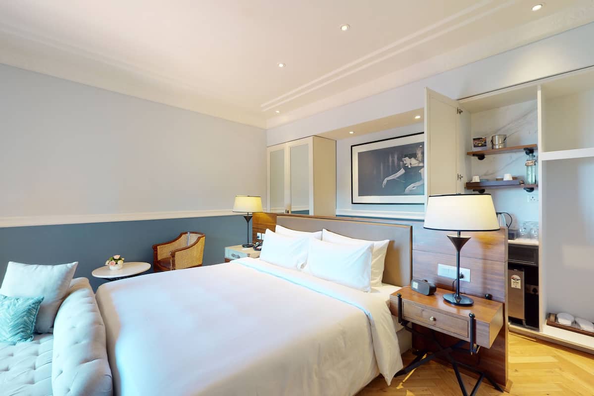 Una habitación de hotel con una cama grande, mesitas de noche, un armario y un cuadro enmarcado en la pared.