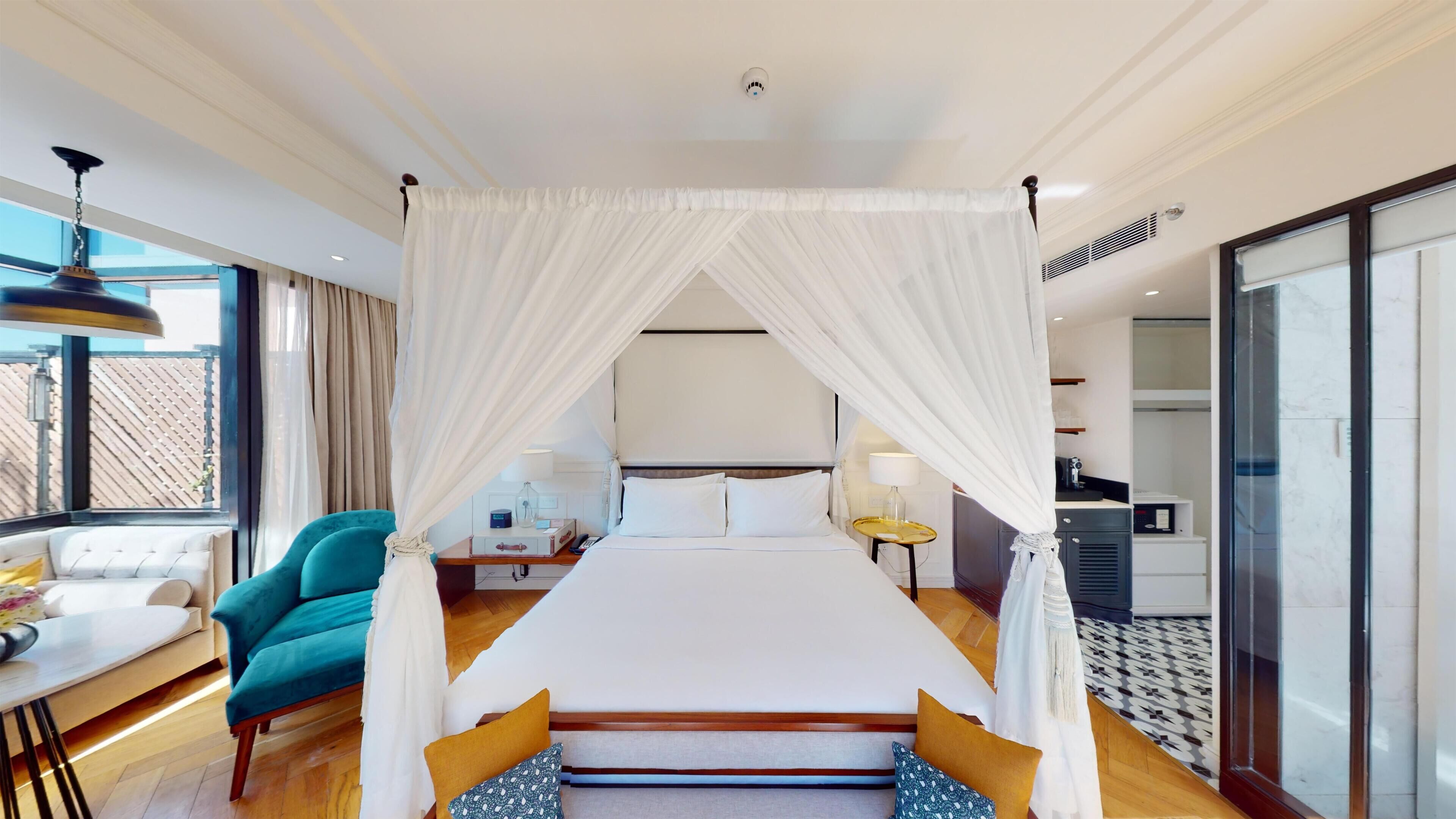 A hotel room with a canopy bed, a desk with a chair, a sofa, and a view of the outside.