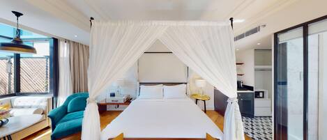 A hotel room with a canopy bed, a desk with a chair, a sofa, and a view of the outside.