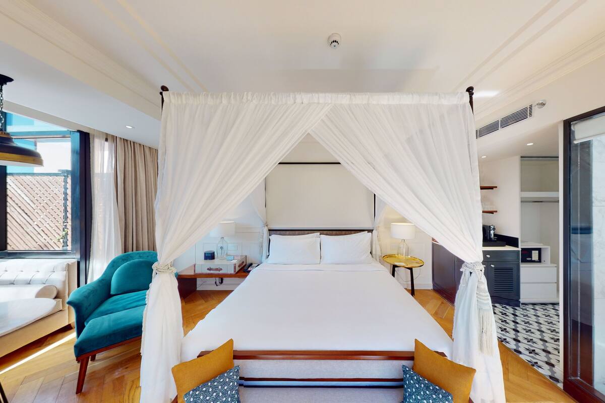 Habitación de hotel con una cama grande, un área de descanso con sofá y sillones, una mesita y vistas al exterior.