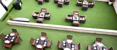 Une terrasse sur le toit dotée de plusieurs espaces de détente, comprenant des tables rondes et des canapés, aménagés sur une pelouse artificielle.