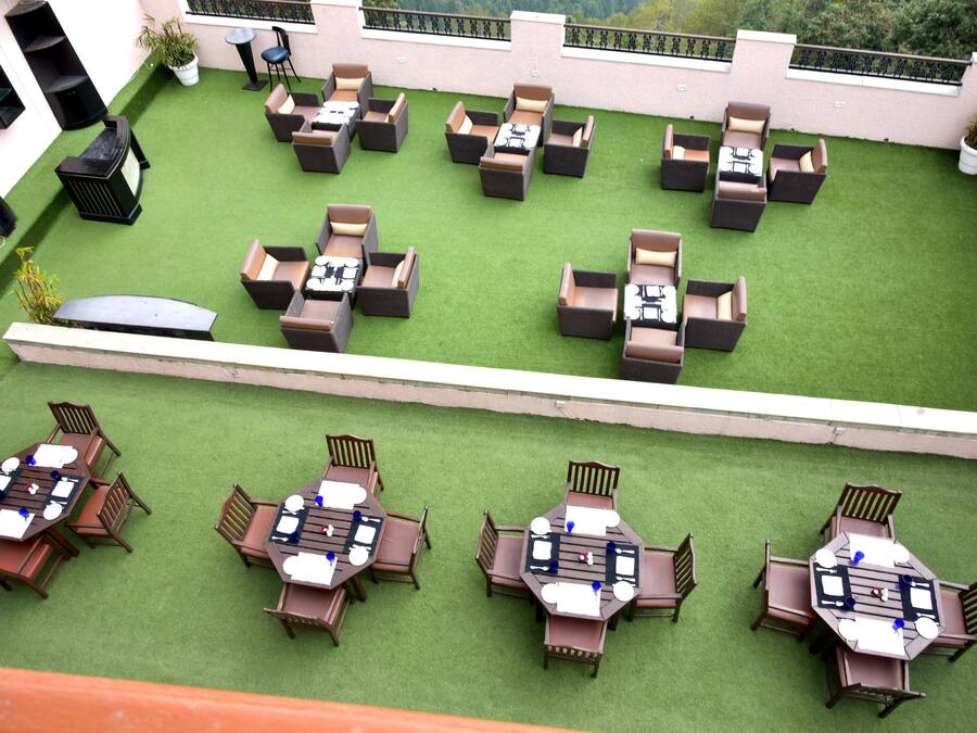 Een terras op het dak met verschillende zithoeken, waaronder ronde tafels en banken, aangelegd op kunstgras.
