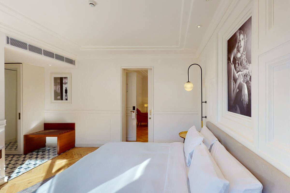 Habitación de hotel con una cama grande, un banco de madera, un cuadro enmarcado y una lámpara moderna.