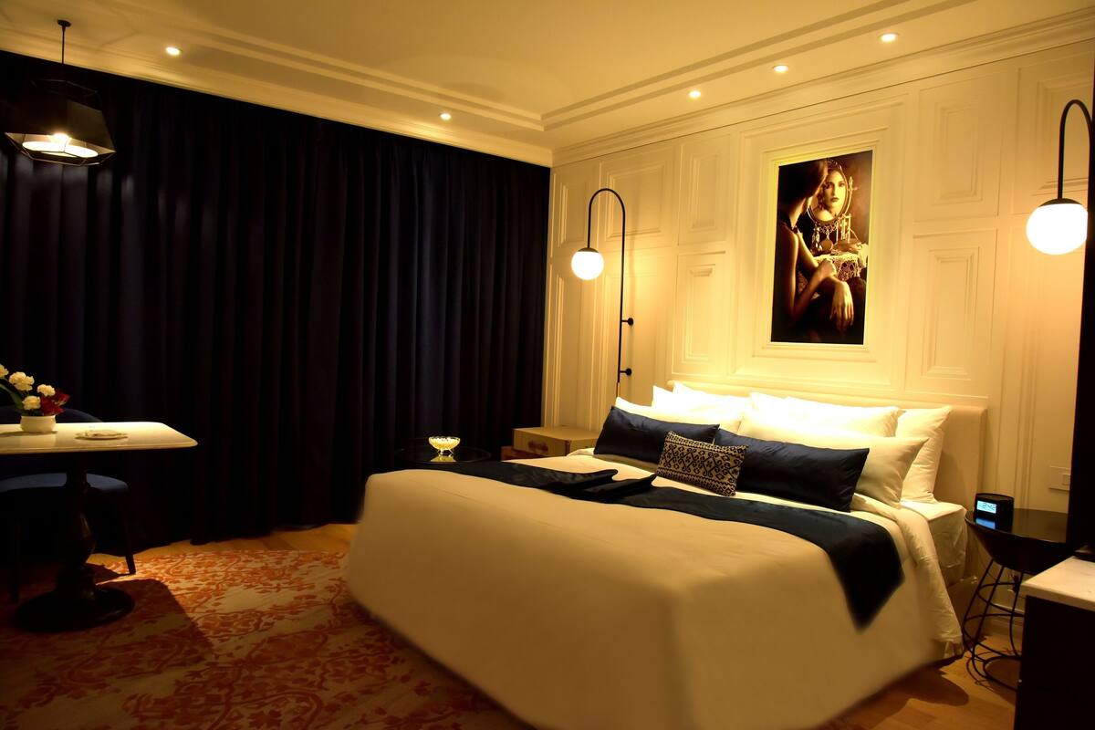 Una habitación de hotel con una cama grande, un escritorio, una silla, una mesa con flores y un cuadro en la pared.