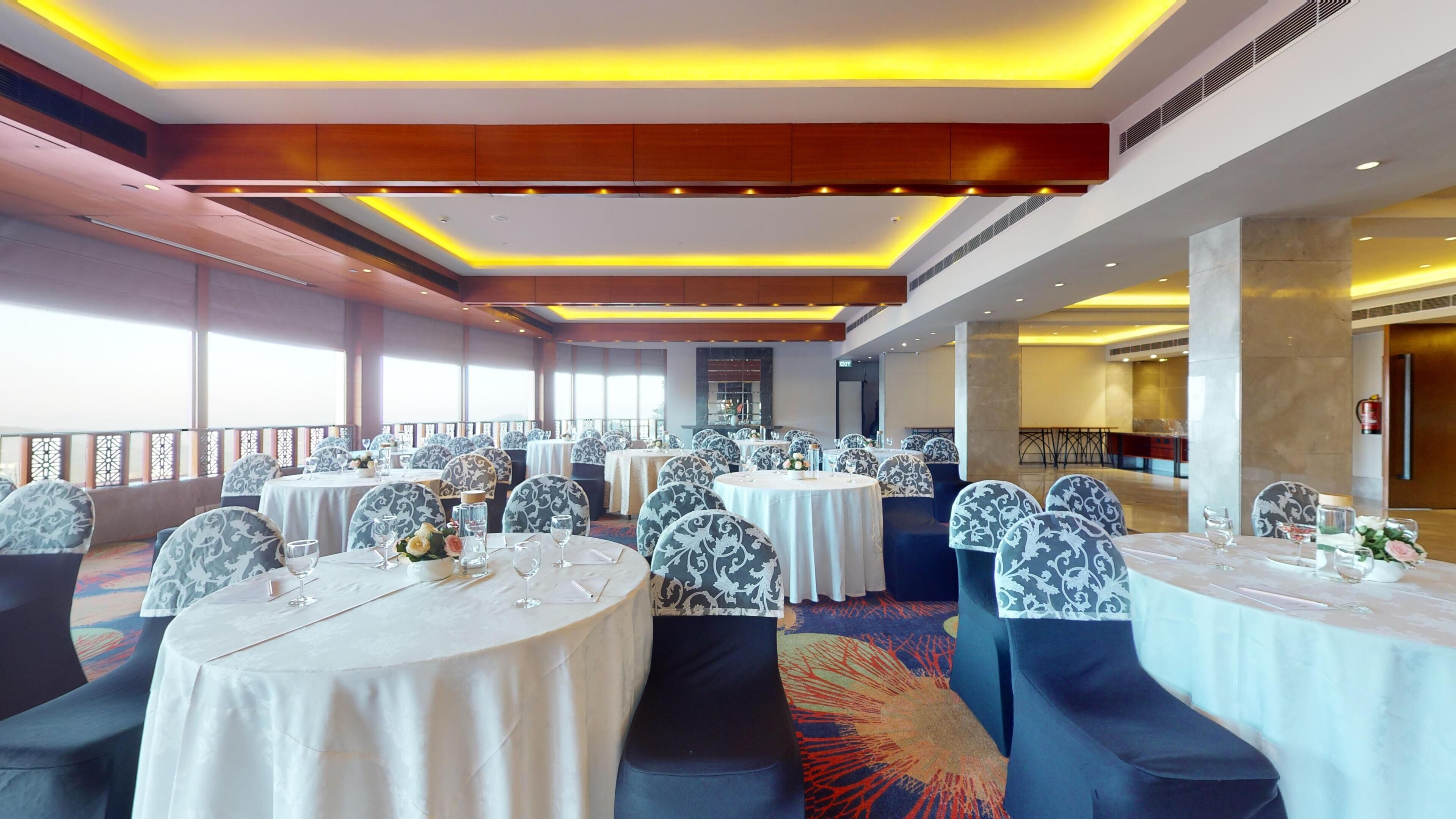A banquet hall with round tables, patterned chairs, and a view of the outdoors.