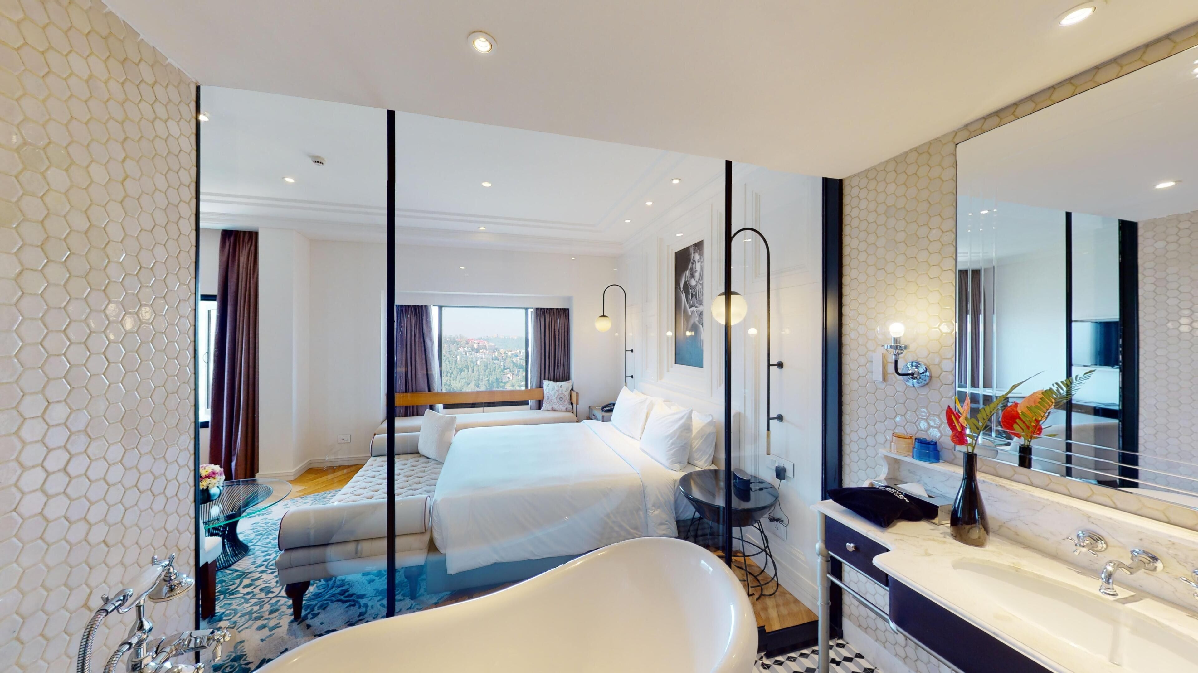A hotel room with two beds, a large mirror, a bathtub, and a view of the city.