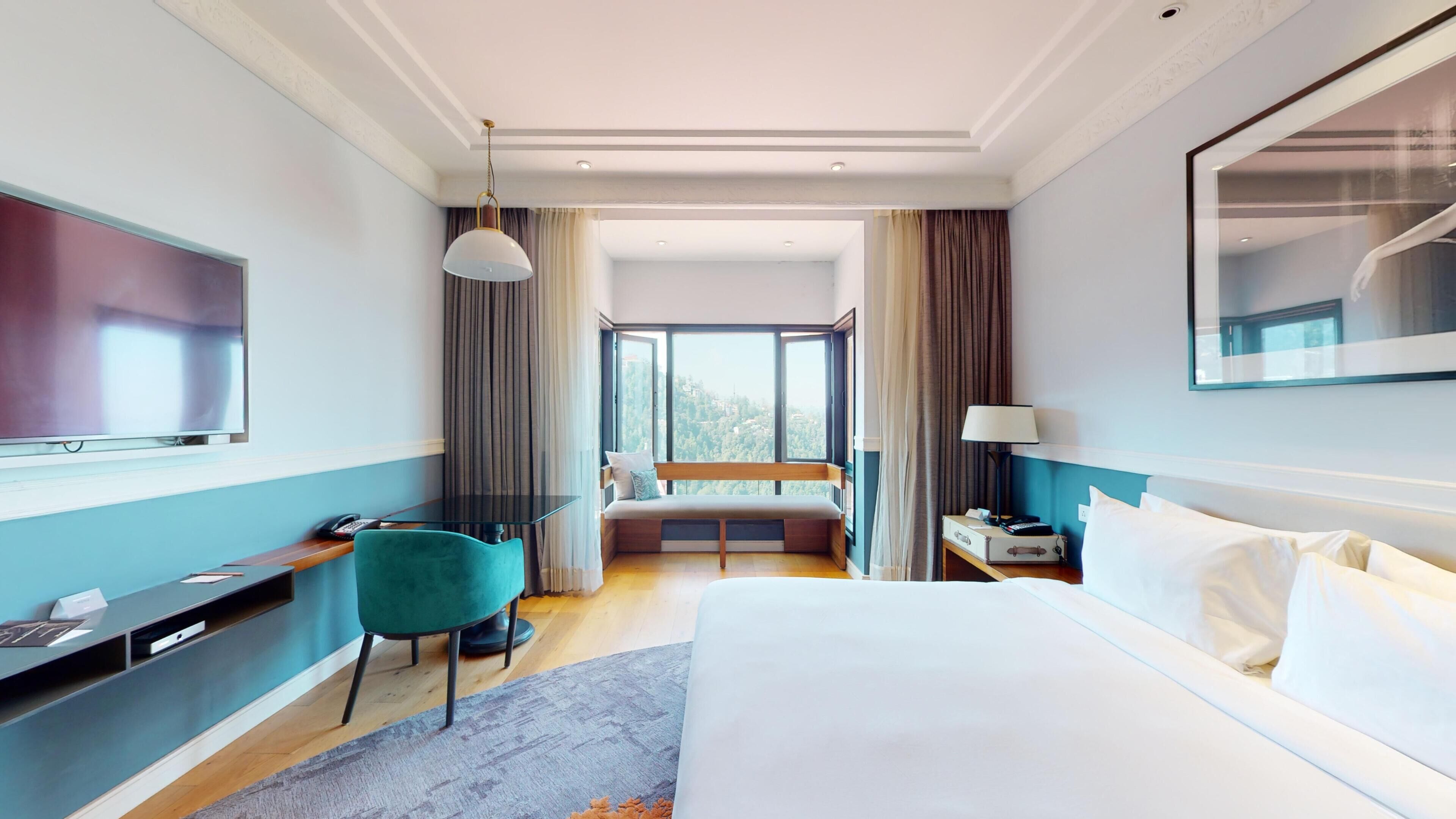 Una camera d'albergo con un letto, una scrivania, una sedia, una televisione, una finestra con tende e una lampada.