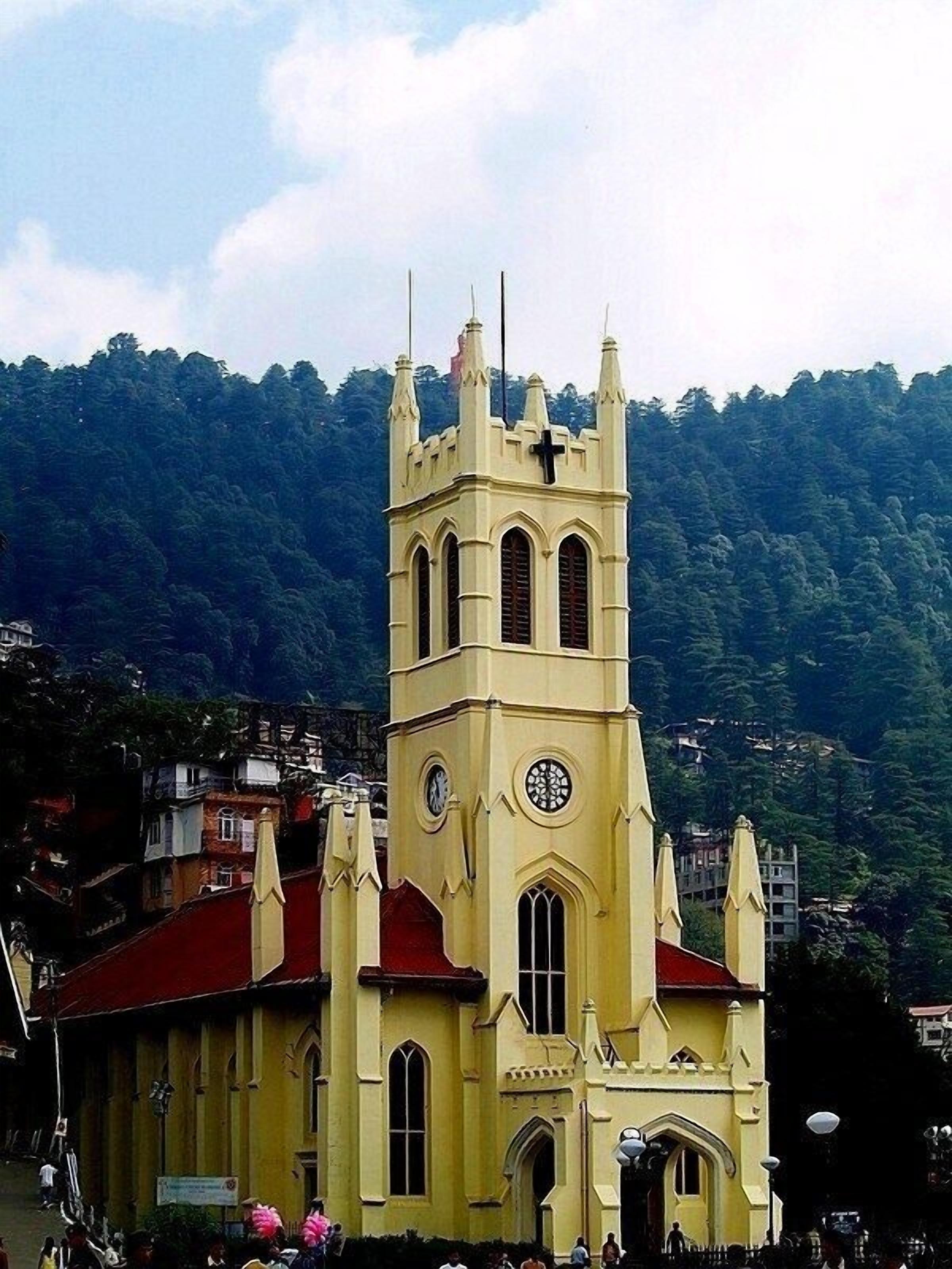 A church with a clock tower, red roof, and a mountainous backdrop.