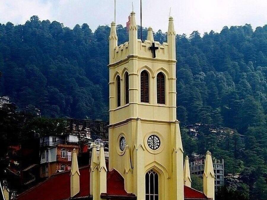 A church with a clock tower, red roof, and a mountainous backdrop.