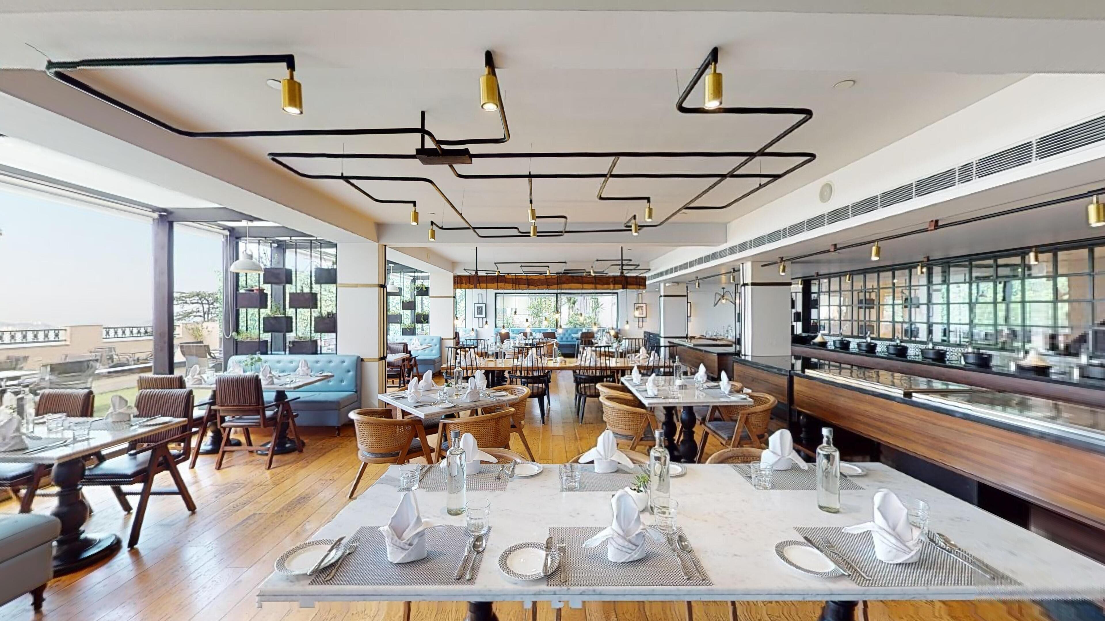 Un restaurante moderno con techos altos, conductos expuestos y una variedad de asientos, incluyendo mesas y cabinas.