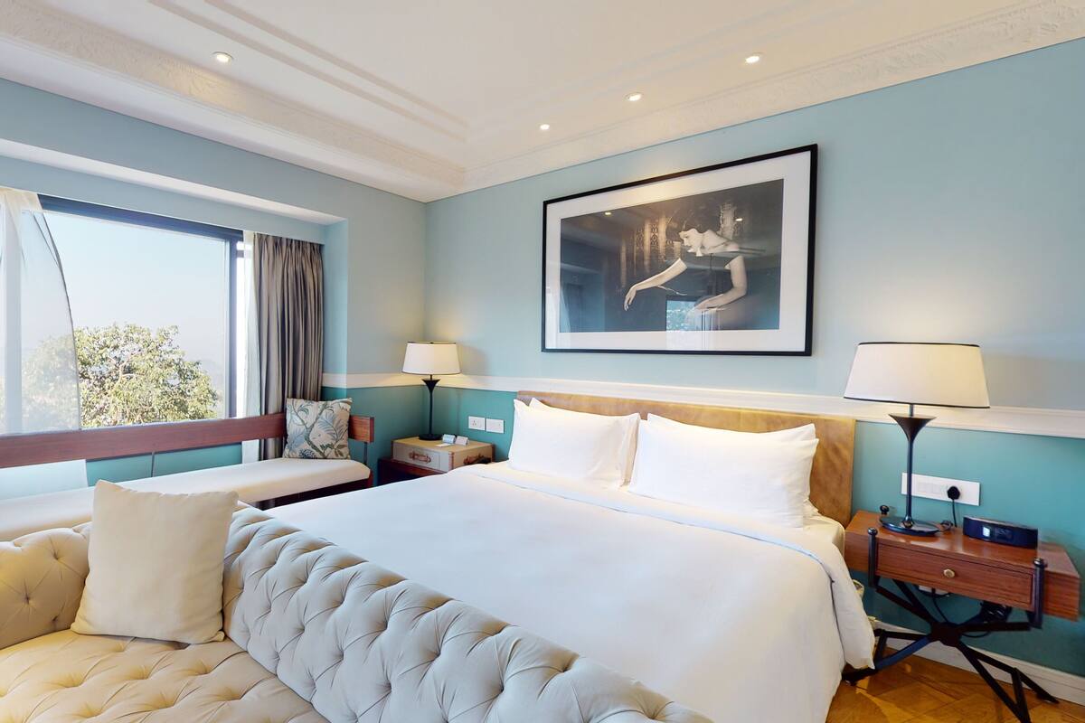 Habitación de hotel con una cama grande, un banco, una mesita de noche, una lámpara y un cuadro en la pared.
