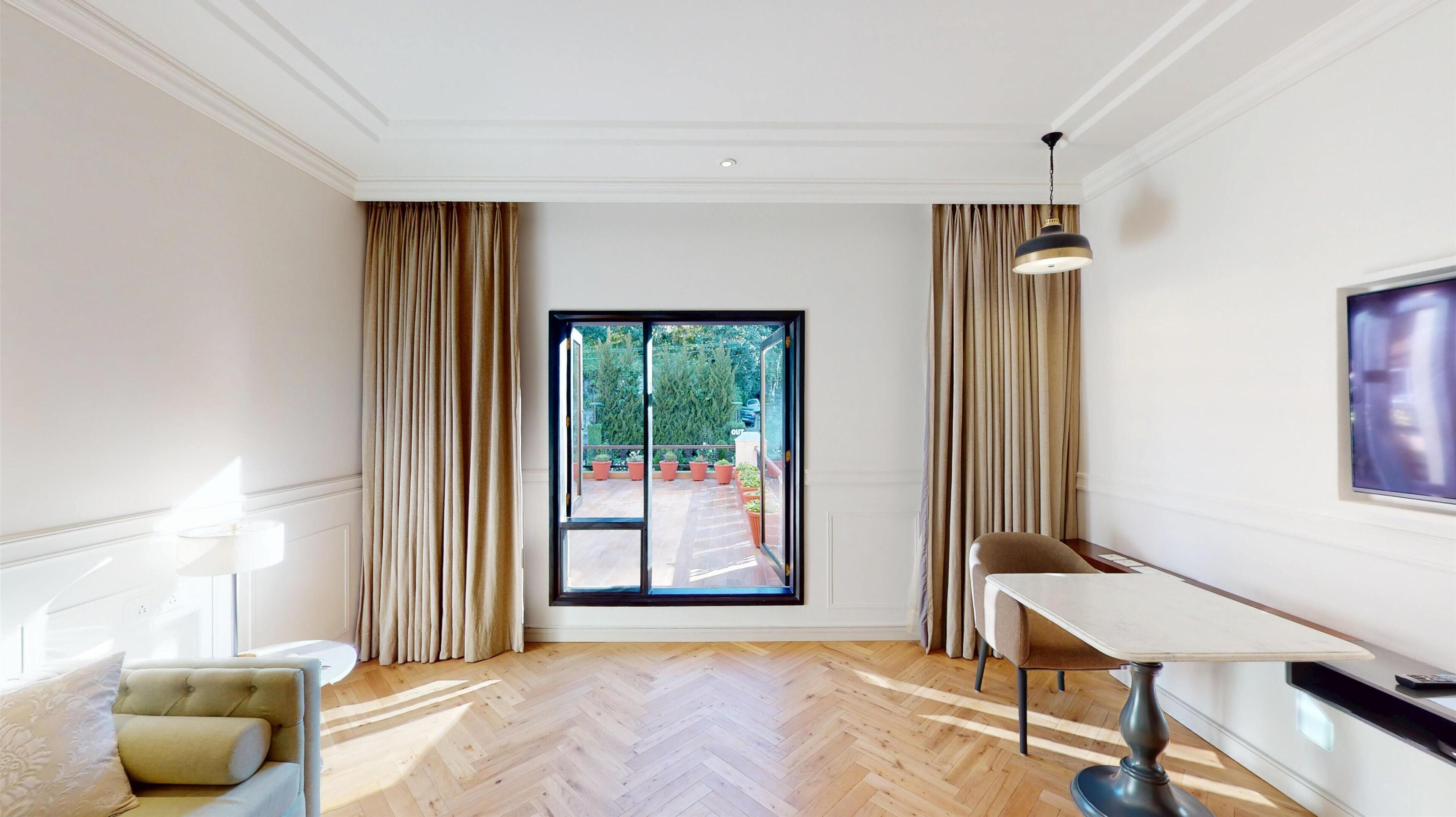 Una habitación de hotel moderna con un amplio ventanal corredero que da a un balcón, una mesa de comedor con una silla y un televisor montado en la pared.