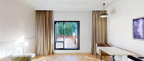 Una habitación de hotel moderna con un amplio ventanal corredero que da a un balcón, una mesa de comedor con una silla y un televisor montado en la pared.