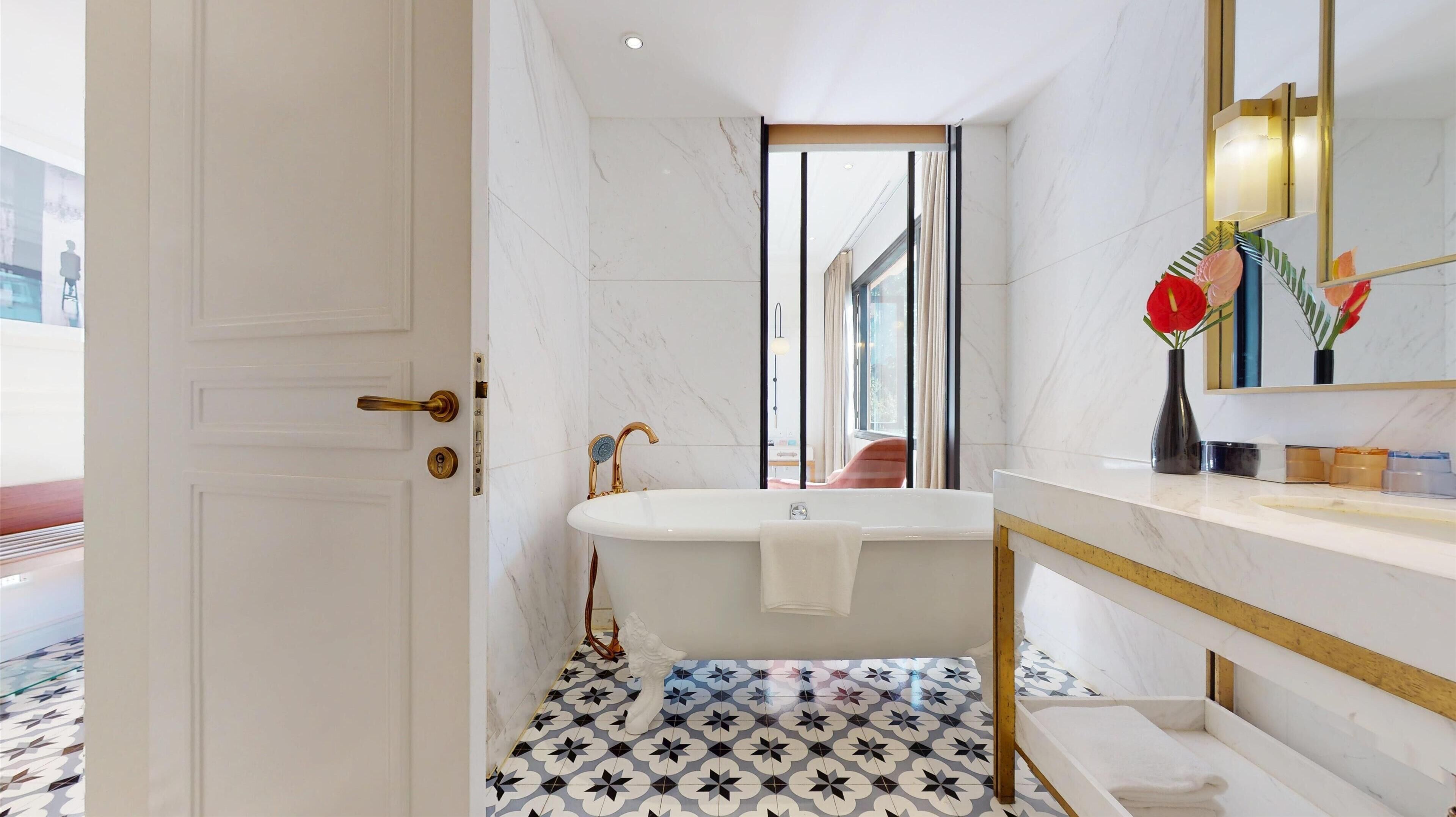 A modern bathroom with a freestanding bathtub, a marble floor, and a large mirror with a gold frame.