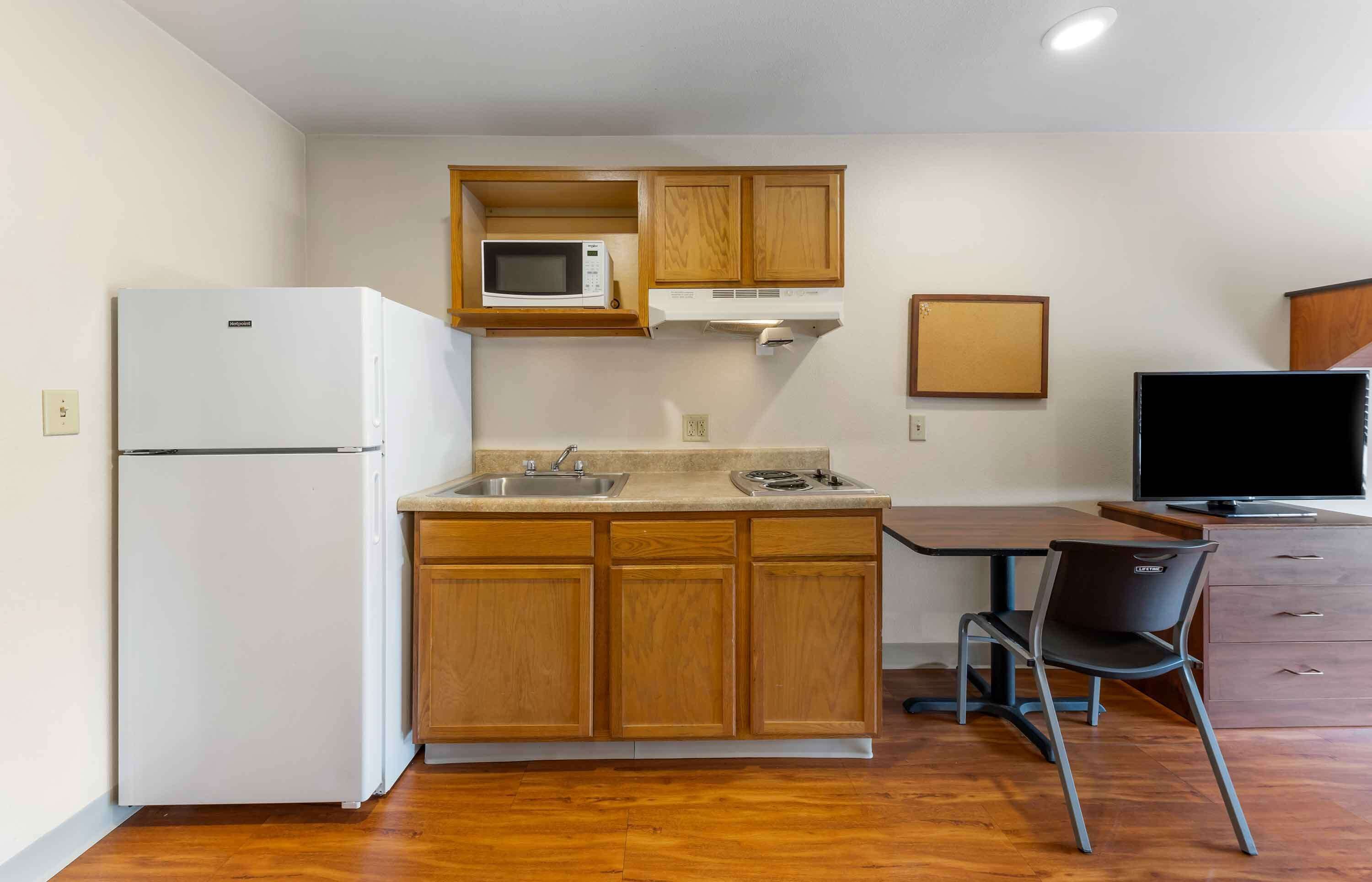Cocina compacta con refrigerador, microondas, pileta y un pequeño comedor con una silla y una mesa.