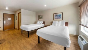 Habitación de hotel con dos camas individuales, piso de madera, una puerta, una ventana con persianas y aire acondicionado instalado en la pared.